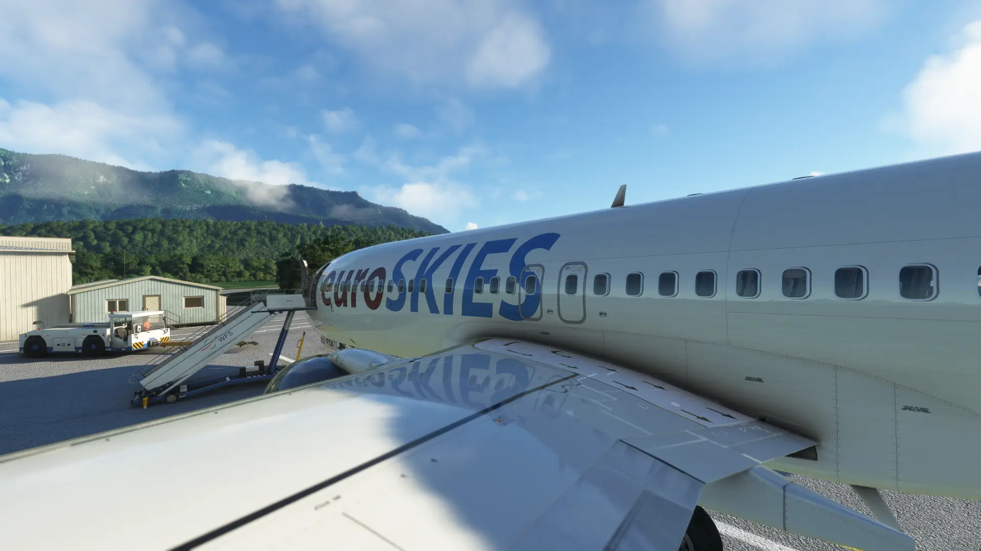 EuroSKIES virtuelles Flugzeug steht am Boden mit Treppenanschluss auf dem Vorfeld, umgeben von Wald und Bergen.